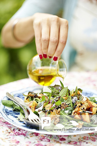 Eine Frau gibt mit der Hand Öl in den Salat