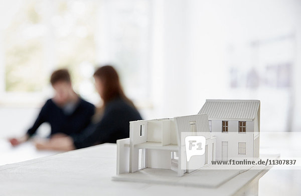 Architekturmodell eines Gebäudes mit zwei Personen bei einem Treffen  das im Hintergrund unscharf abgebildet ist. Kommunikation.