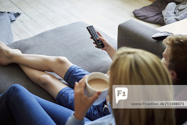 A woman sitting with a cup of tea holding the television remote control in her hand.