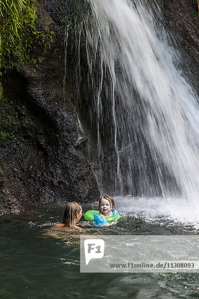 Mutter mit Tochter schwimmen unter Wasserfall