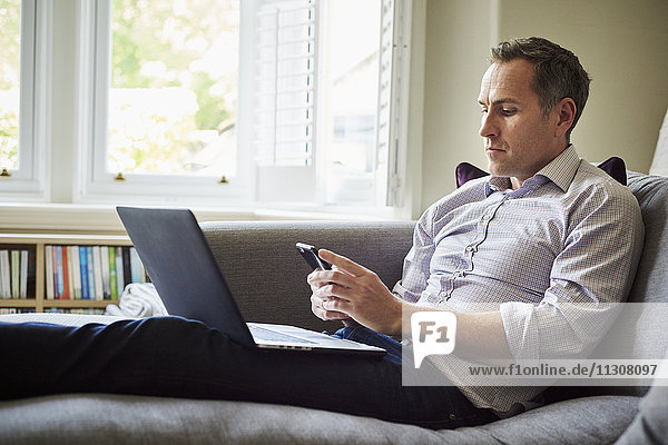 A man seated on a sofa at home using a laptop.