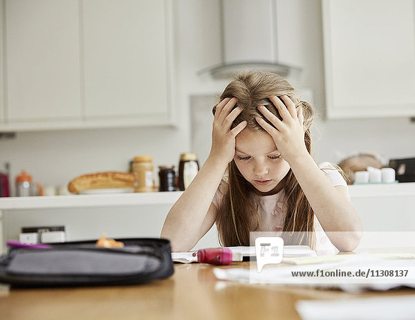 Ein Mädchen sitzt an einem Tisch mit den Händen auf dem Kopf und schaut auf ihre Hausaufgaben.