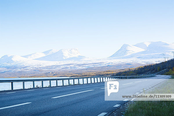 Empty road with snowcapped mountains on background
