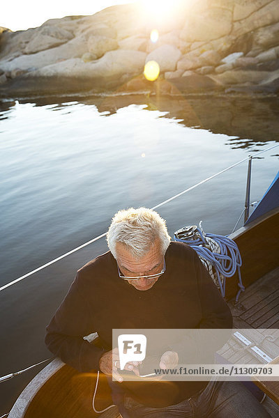Älterer Mann auf einem Boot benutzt ein Mobiltelefon