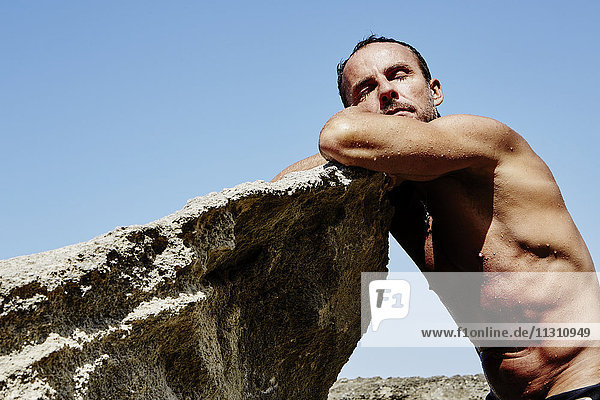 Mann lehnt an einem Felsen am Strand