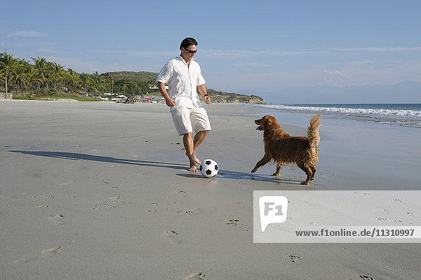 Mann spielt mit seinem Hund am Strand