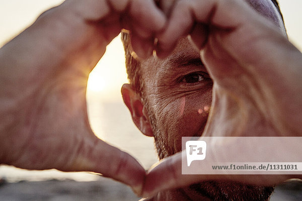 Porträt eines Mannes  der am Strand ein Herz formt