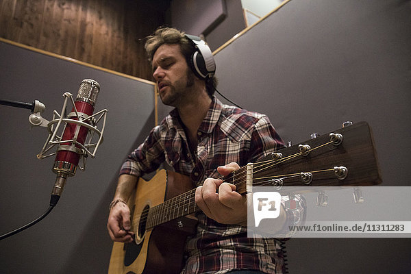 Mann spielt Gitarre in einem Aufnahmestudio während einer musikalischen Aufnahme