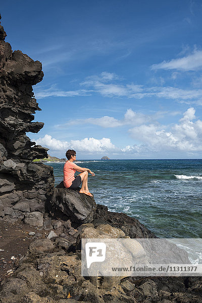 USA  Hawaii  Molokai  Frau sitzt auf einer Klippe an der Südostküste MR