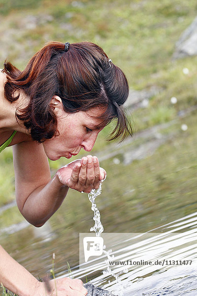 Frau trinkt Wasser aus einem Teich