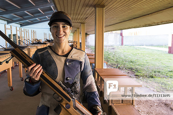 Porträt einer lächelnden Frau  die ihr Sportgewehr in einem Schießstand hält.