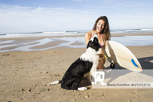 Glückliche Frau mit Hund und Surfbrett am Strand