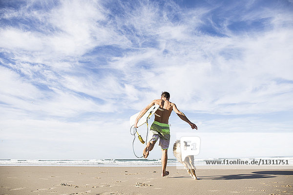 Mann mit Surfbrett und Hund am Strand