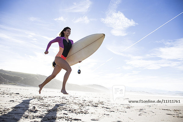 Woman carrying surfboard running on the beach