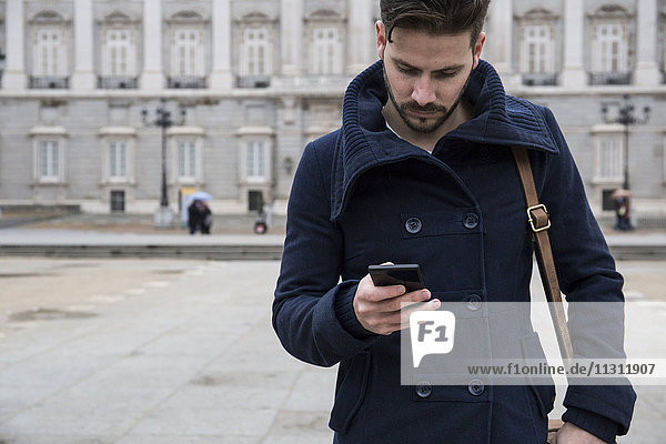 Man with a coat and bag using his phone