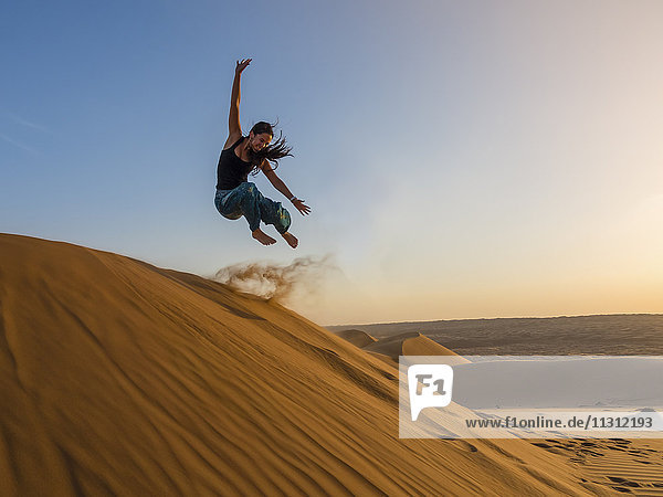 Oman  Al Raka  Young woman jumping from dune in Rimal Al Wahiba desert