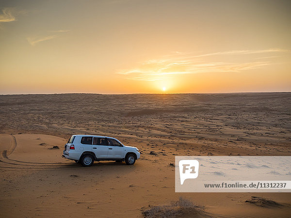 Oman  Al Raka  off-road vehicle parking on dune in Rimal Al Wahiba desert at sunset