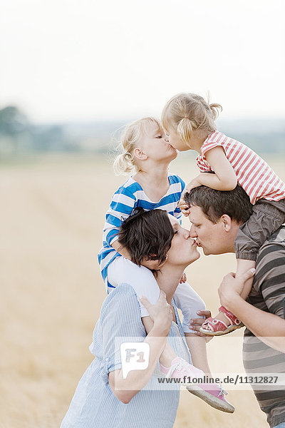Family with two children kissing in field