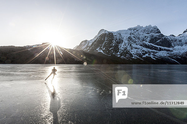 Mann beim Schlittschuhlaufen auf zugefrorenem See bei Sonnenuntergang