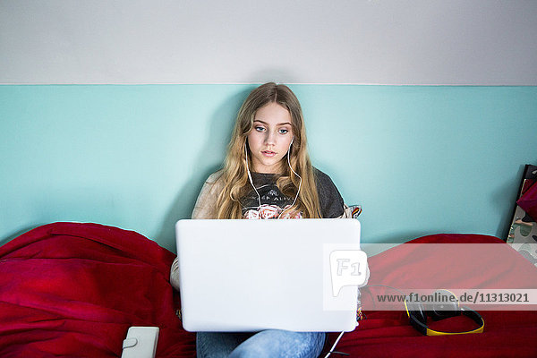 Junge Frau sitzt auf dem Bett und benutzt einen Laptop