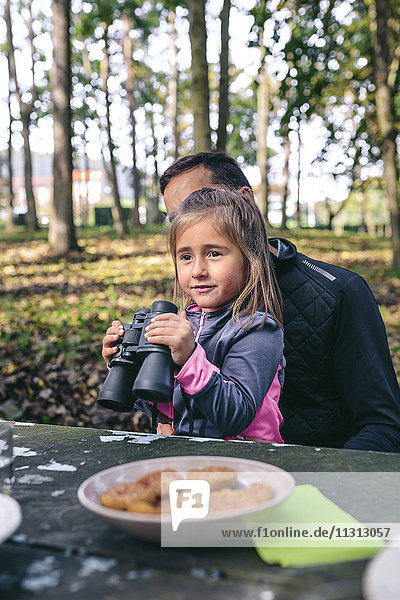 Little girl with binocular relaxing with her father in a forest