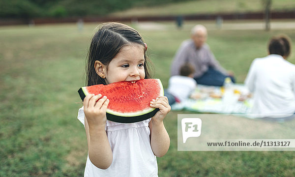 Mädchen essen Wassermelonenscheibe mit ihrer Familie im Hintergrund