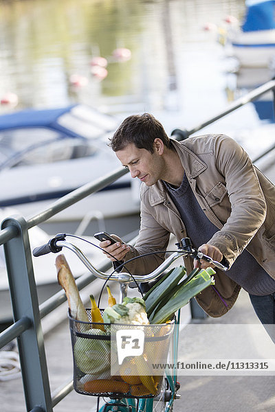 Mann lehnt an seinem Fahrrad und schreibt eine SMS mit seinem Handy