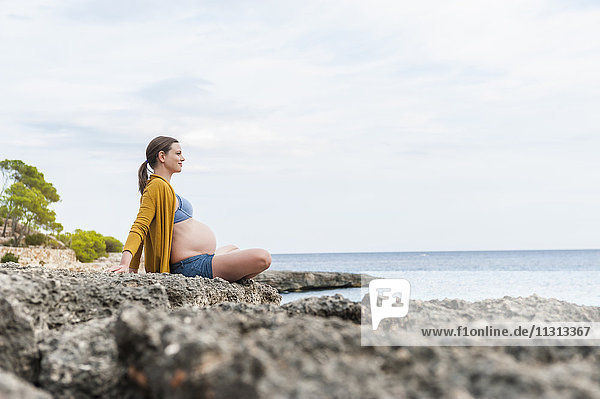 Schwangere Frau auf Felsen am Meer sitzend