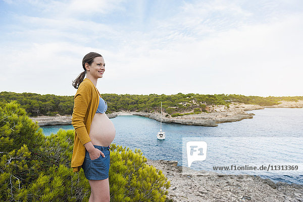 Lächelnde schwangere Frau am Meer stehend