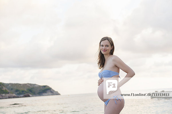 Lächelnde schwangere Frau am Strand stehend
