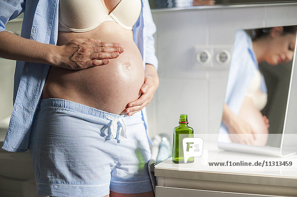 Schwangere Frau im Badezimmer  die Öl auf ihren Bauch aufträgt.