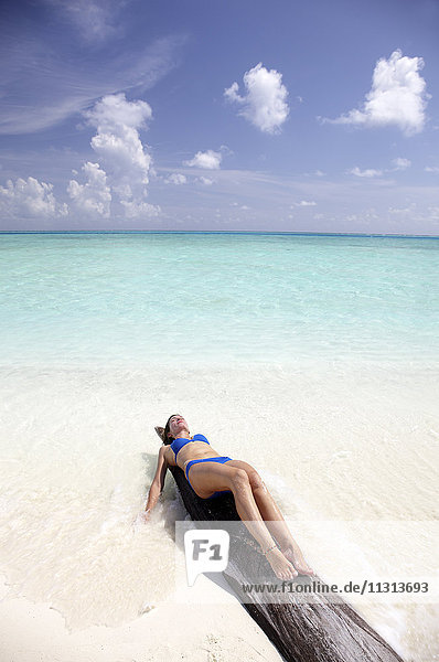 Malediven  Frau beim Sonnenbaden auf einem Baumstamm am Strand