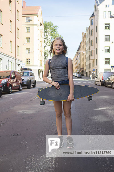 Mädchen steht auf der Straße und hält ein Skateboard