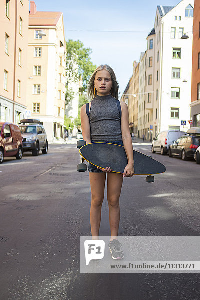 Mädchen steht auf der Straße und hält ein Skateboard