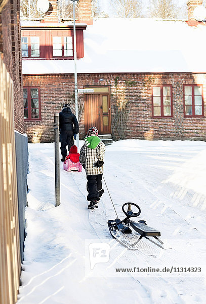 Rear view of woman with children walking and pulling sleigh