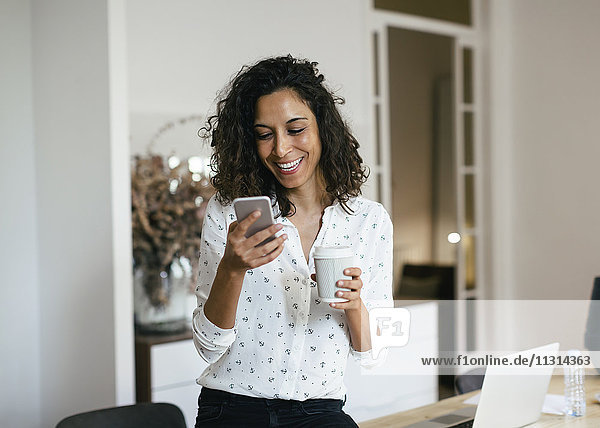 Businesswoman in office using smart phone  holding cup of coffee