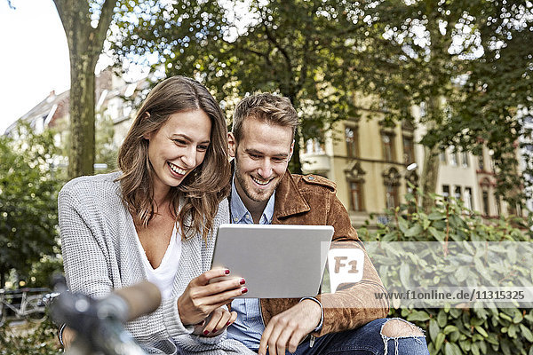 Smiling young couple using tablet in park