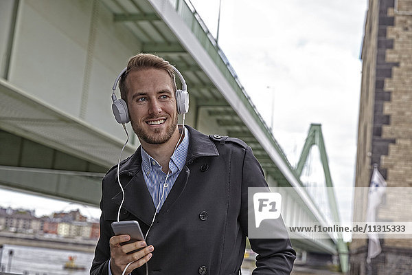 Lächelnder junger Mann mit Kopfhörer und Handy im Freien