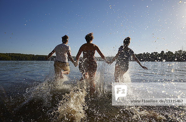 Back view of friends running in a lake