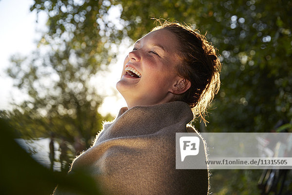 Lachende junge Frau in eine Decke gewickelt bei Sonnenuntergang