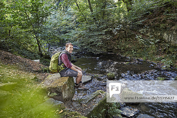 Hiker in forest sitting on rocks at a brook