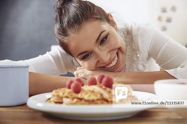Porträt einer glücklichen jungen Frau  die in der Küche auf Waffeln schaut.