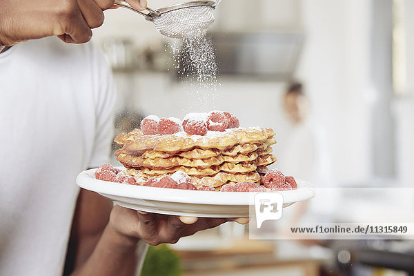 Young man sprinkling icing sugar on stack of waffles  close-up