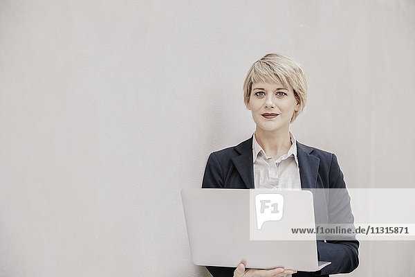 Geschäftsfrau mit Laptop vor der Betonwand