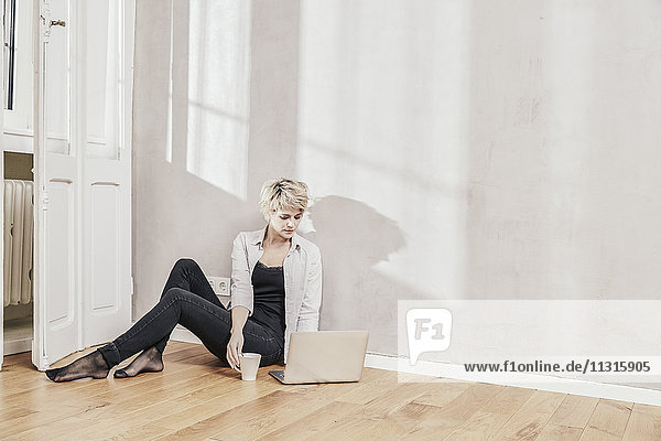 Frau auf dem Boden sitzend mit Kaffeetasse und Laptop
