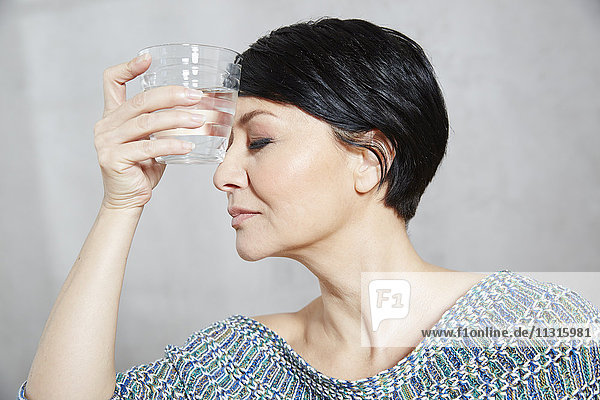 Woman holding glass of water to her forehead