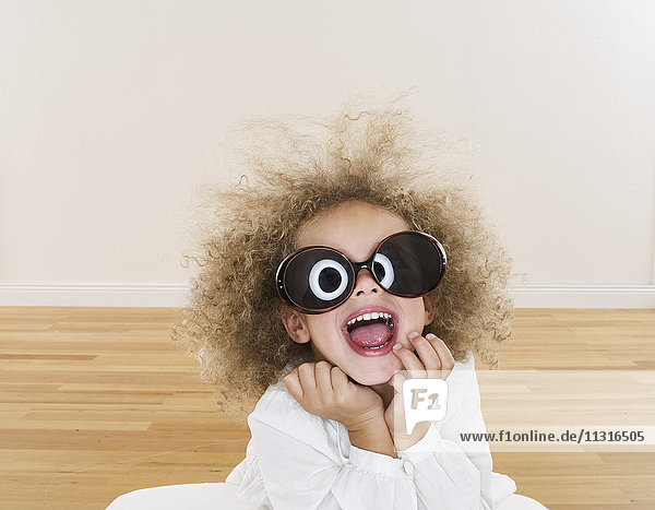 Porträt eines lächelnden Mädchens mit blonden Ringeln und übergroßer Sonnenbrille