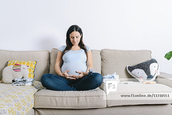 Schwangere Frau sitzt auf der Couch und hält den Bauch.