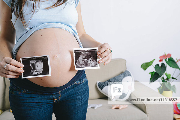 Pregnant woman holding ultrasound images in front of belly