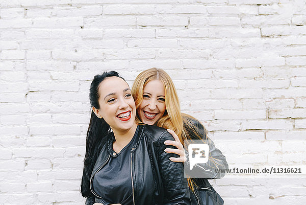 Zwei lachende junge Frauen vor weißer Ziegelwand